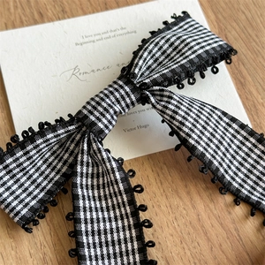 Détail d'une pince à cheveux à nœud vichy noir et blanc avec bordure à anneaux décoratifs