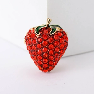 Close-up of strawberry brooch with red rhinestones and green metal leaves on a white stand