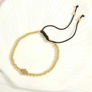 Detail of gold beaded bracelet with Hamsa Evil Eye charm on adjustable black cord