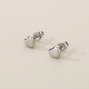 Gros plan de boucles d'oreilles cœur en acier inoxydable poli argenté sur fond beige