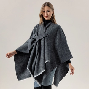 Detail of dark grey knit poncho featuring fringe edges and soft cashmere-like texture