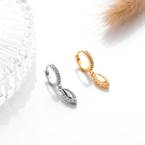 Close-up of gold and silver hoop earrings with hollow teardrop pendants and zircon stones