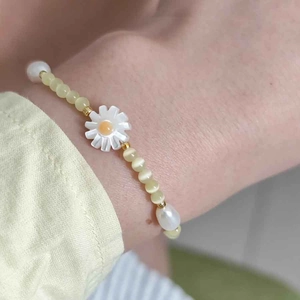 Close-up of beaded bracelet with cat eye stones, pearls and a daisy pendant