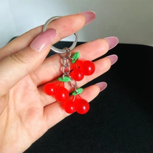 Close-up of translucent red resin cherry keychain with green leaves on black background