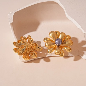 Détail de boucles d'oreilles fleurs en or mat avec perle violette et métal brossé