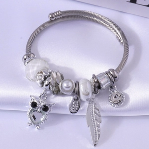 Silbernes Armband mit Eulen- und Federanhängern auf weißem Satinhintergrund präsentiert