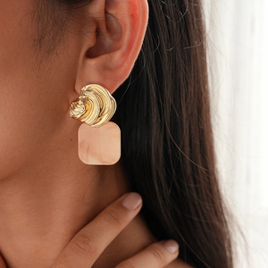 Close-up of gold swirl metal earring with square pink resin pendant worn by a model