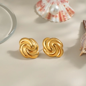 Detail of twisted spiral gold earrings on beach-themed decor with shells and pearls