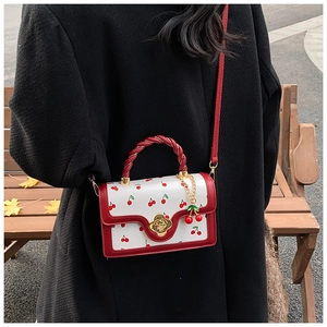 Detail of white crossbody bag with cherry prints, floral gold clasp, and braided handle