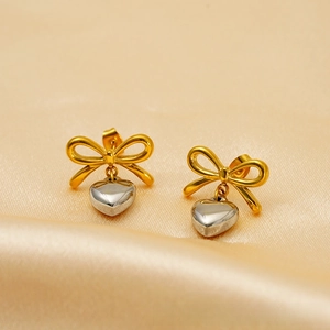 Macro view of gold bow and silver heart pendant stud earrings on silk background