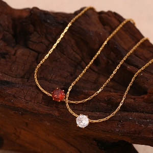 Detail of 18K gold plated thin chain necklaces with red and white zircon pendants on wood