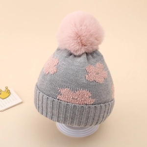 Close-up of winter knit baby hat with pink flower detail and fluffy pom-pom