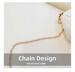 Detail showing high-quality golden metal chain strap on a white textured mini shell bag