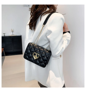Quilted black chain crossbody bag with golden heart lock worn over a white blazer