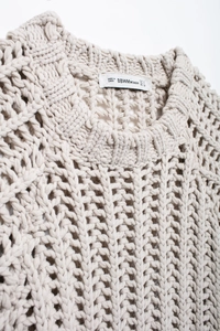 Gros plan sur le col d'un pull en grosse maille beige révélant la texture ajourée et l'étiquette