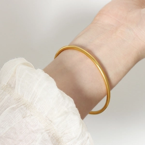 Minimalist gold plated titanium steel bangle shown on a wrist with white textured cuff