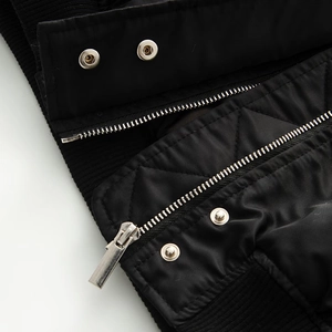 Detail showing silver metal zipper, snap button and black ribbed cuff on bomber jacket