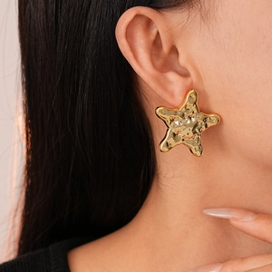 Macro detail of large gold-tone textured starfish earrings worn by a model in luxury style