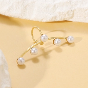 Detailed view of a gold ear cuff featuring five elegant white pearls on a stone background