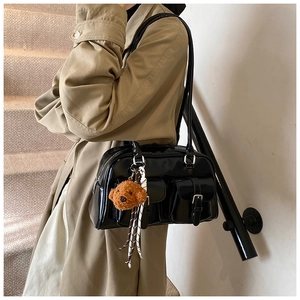 Detail of black patent leather shoulder bag with silver buckles and brown plush bear charm