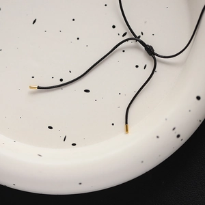 Macro detail of black cord necklace with adjustable knot and golden metal ends on ceramic