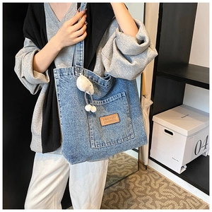 Detail of blue denim tote bag with leather logo patch and white plush cloud pendant
