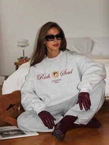 Λεπτομέρεια από γκρι oversized φούτερ με στάμπα 'Rich Soul' σε άνετο εσωτερικό περιβάλλον