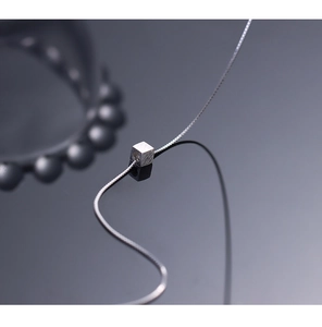 Macro shot of silver cube pendant with brushed metal texture and sleek snake chain