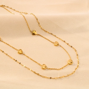 Double-layered gold stainless steel necklace with heart pendant on beige fabric