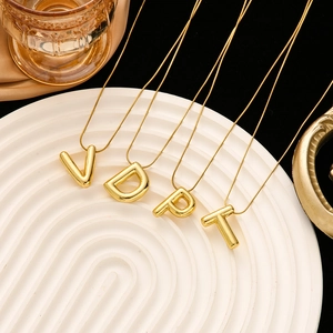 Close-up of gold 3D initial letter pendants with snake chains on a white ripple plate