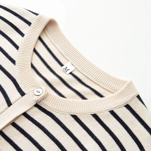 Vue détaillée du col rond avec bouton et motif à rayures sur le pull en maille beige