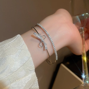 Close-up of a silver bow cuff bracelet and a sparkling tennis chain set on a wrist