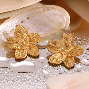 Macro shot of gold floral earrings with brushed texture on a reflective water surface