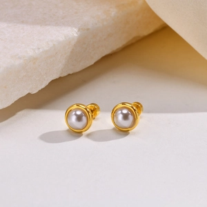 Detailed view of elegant gold pearl earrings on a textured stone and soft fabric base