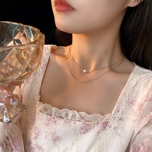 Detail of layered gold necklace with pearl and metal tube pendant on elegant model