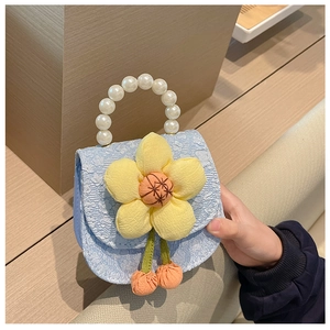 Close-up of blue textured bag with yellow flower, pearl handle, held by a child hand