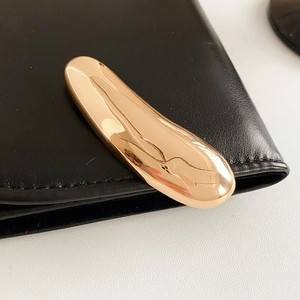 Close-up of a minimalist golden polished metal brooch pinned on black leather texture