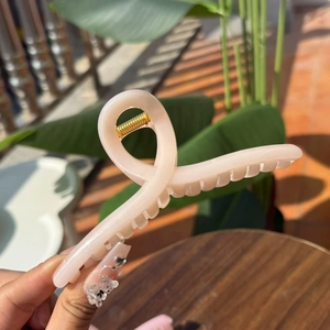 Detail showing creamy pink resin hair claw clip with golden spring on wooden table