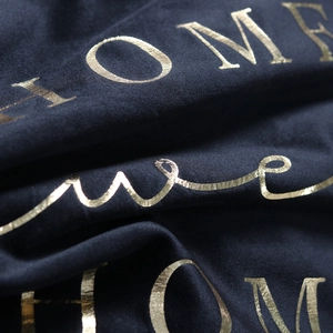 Close-up of golden HOME lettering on dark velvet pillowcase fabric with luxury texture