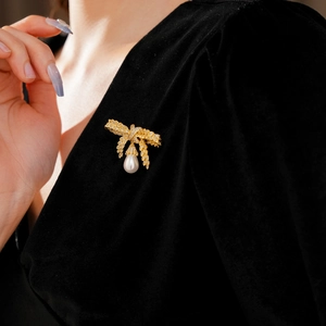 Détail d'une broche noeud doré avec perle goutte sur tissu velours noir