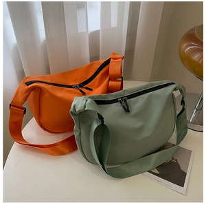 Detail of orange and grey-green nylon dumpling crossbody bags on a white table