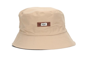 Detail of the reinforced stitched brim and brown logo patch on the beige bucket hat