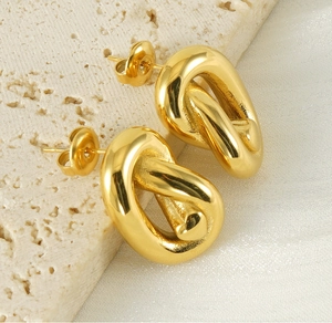Gros plan détaillé de boucles d'oreilles nœuds torsadés plaqué or 18K sur de la soie blanche