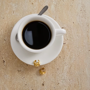 Close-up of golden hoop earrings on a stone surface beside a cup of coffee