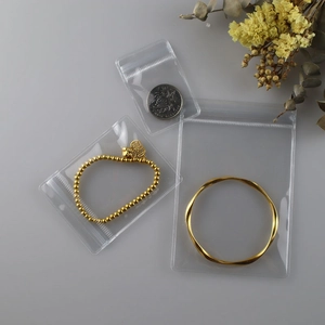Three transparent PVC jewelry storage bags in different sizes on a decorative grey surface