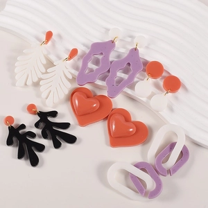 Macro shot of colorful geometric acrylic earrings and resin jewelry pieces on white wavy base