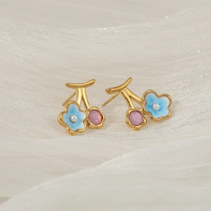 Floral cherry earrings with blue enamel flowers and pink gemstone on white soft fabric