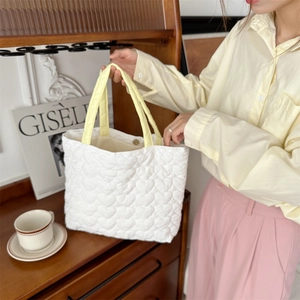 Detail of white heart-quilted tote bag featuring contrasting yellow handles and soft texture