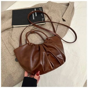 Detail of a brown ruched leather tote bag with a glossy finish and long shoulder strap
