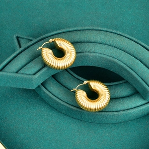 Golden ribbed hollow hoop earrings with textured finish on dark green velvet display